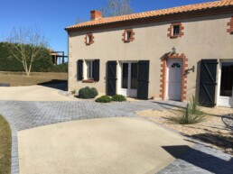 allée d'entrée en béton drainant beige & pavés grès gris. La maison est en enduit beige, contours des ouvertures en briques rouges