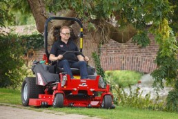 un homme professionel du paysage tond la pelouse sur une tondeuse pneumatique rouge